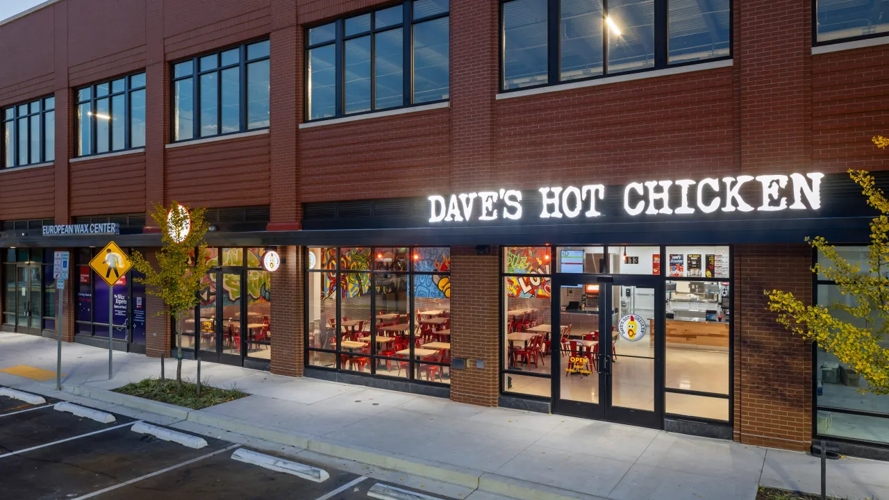 Exterior view of Dave's Hot Chicken on Prosperity Dr, Silver Spring, MD, showcasing vibrant murals and bold signage and large windows.