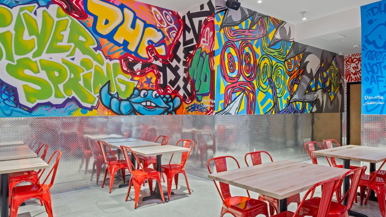 Interior view of Dave's Hot Chicken on Prosperity Dr, Silver Spring, MD, featuring vibrant murals and red seating.