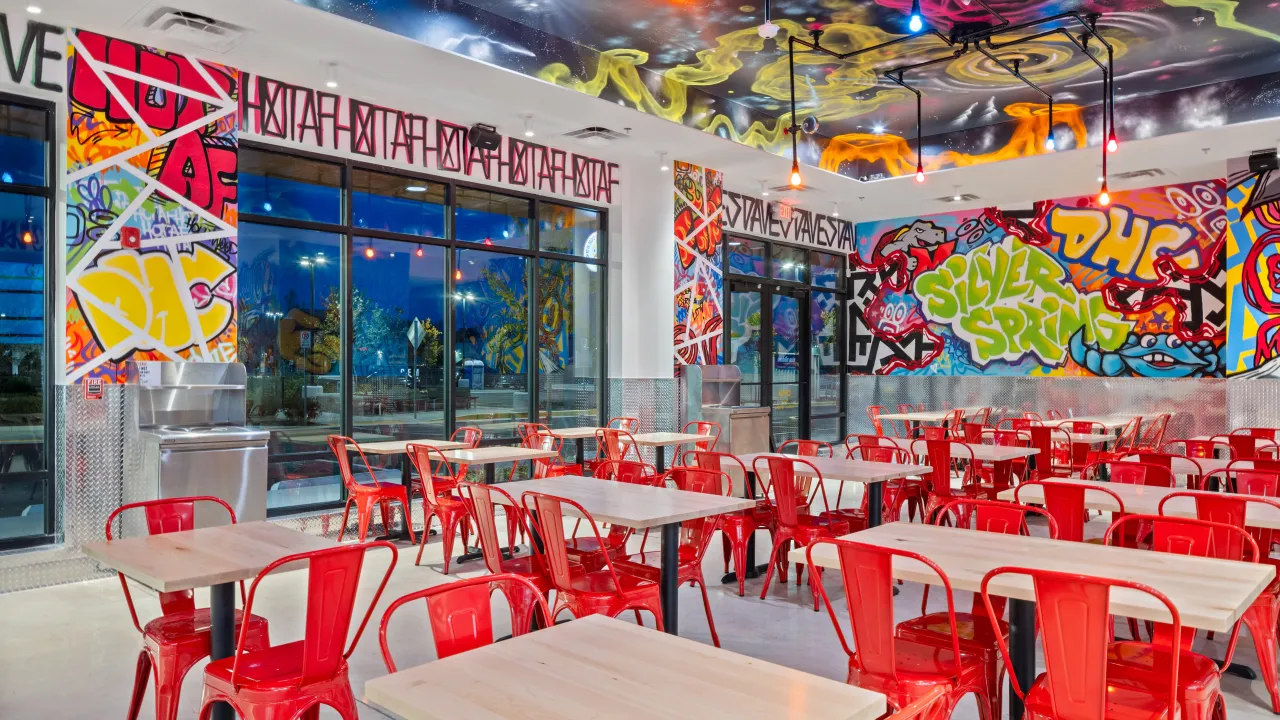 Interior view of Dave's Hot Chicken on Prosperity Dr, Silver Spring, MD, showcasing vibrant murals and red seating and wooden tables.