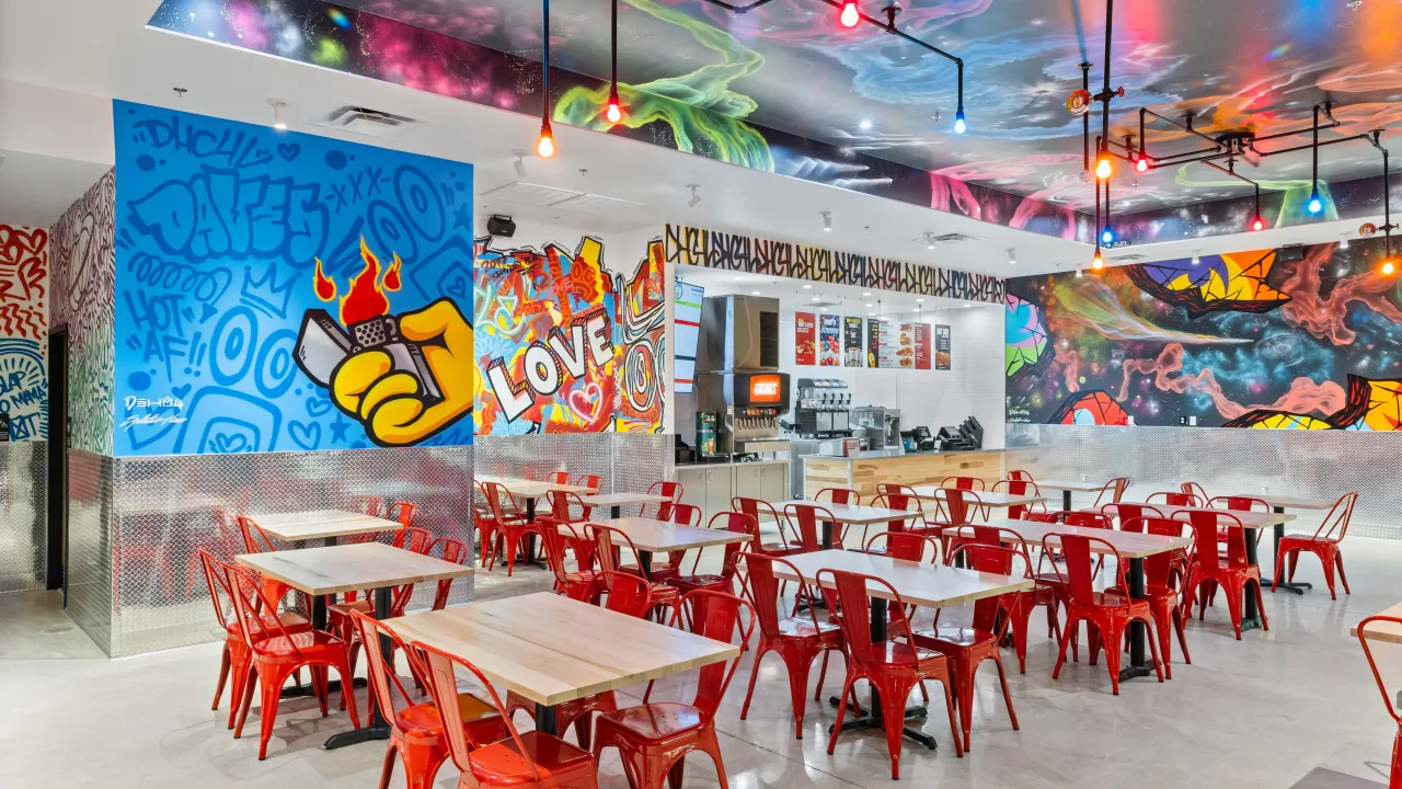 Interior view of Dave's Hot Chicken at 12255 Prosperity Dr, Silver Spring, MD, featuring vibrant wall murals, the counter area and red seating.