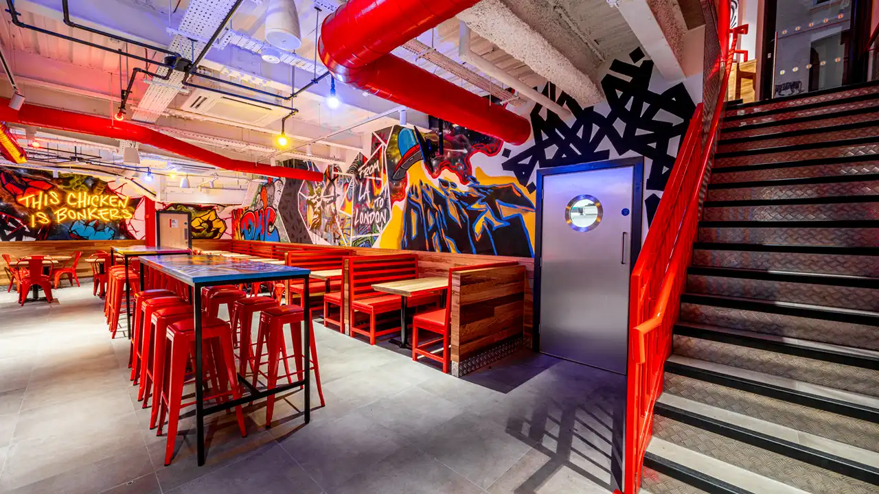 Spacious communal dining area at Dave’s Hot Chicken, London, with graffiti walls, red seating booths, and colorful lighting.