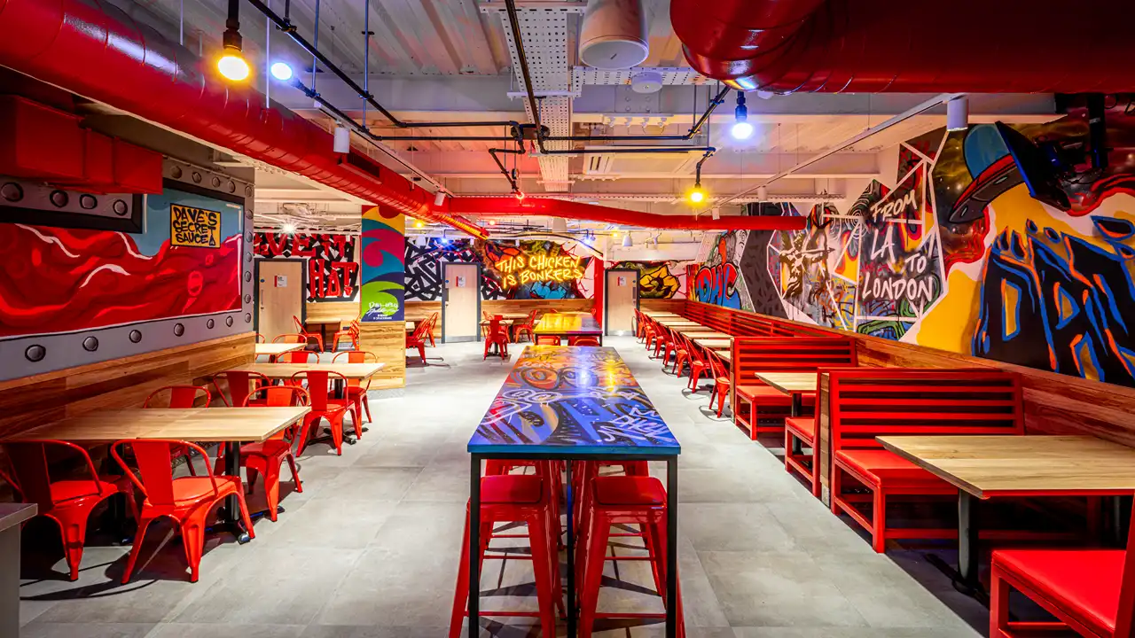 Bright dining area at Dave’s Hot Chicken, Shaftesbury Avenue, London, featuring a mural with the phrase 'From LA to London' and red seating booths.