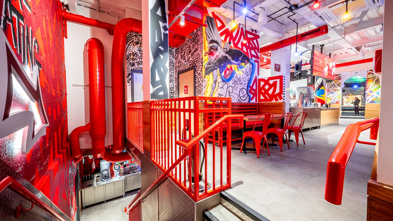 Bold red staircase inside Dave’s Hot Chicken on Shaftesbury Avenue, London, UK, leading to a dining area with artistic graffiti walls and red seating.