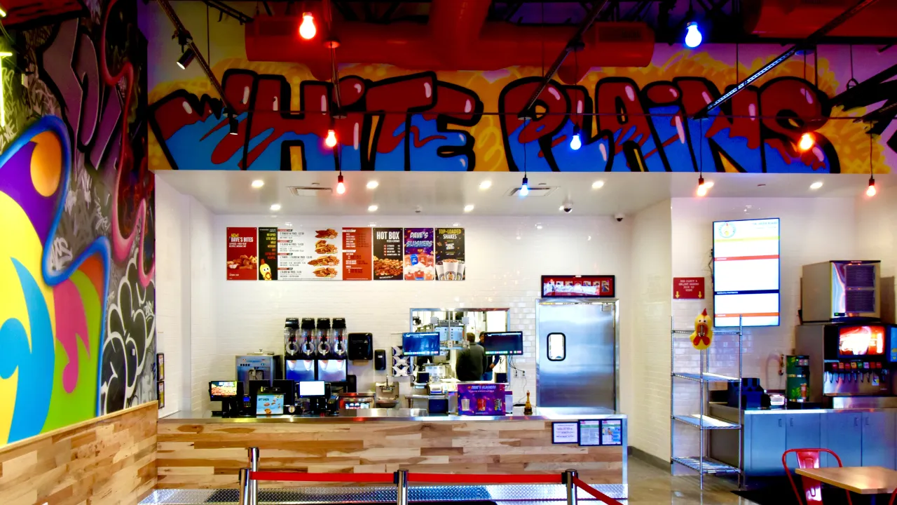 Interior view of Dave's Hot Chicken in White Plains, NY, featuring vibrant murals and a wooden counter.