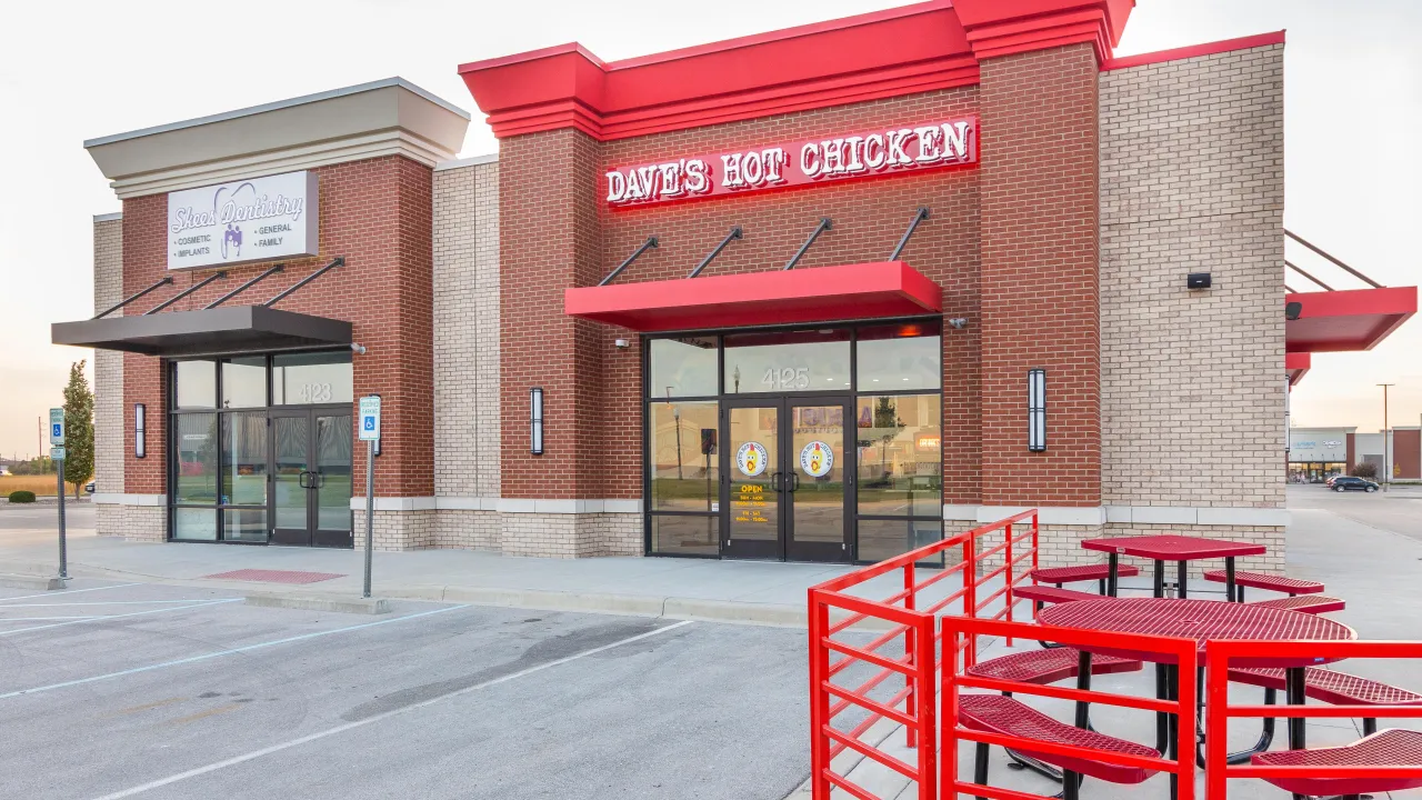 Exterior view of Dave's Hot Chicken at 4125 Town Center Blvd, Jeffersonville, IN, showcasing red signage and outdoor seating.