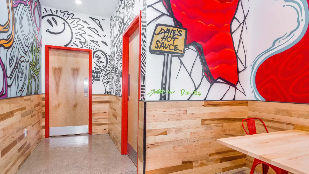 Interior view of Dave's Hot Chicken in Jeffersonville, IN, showcasing vibrant murals and wooden accents.