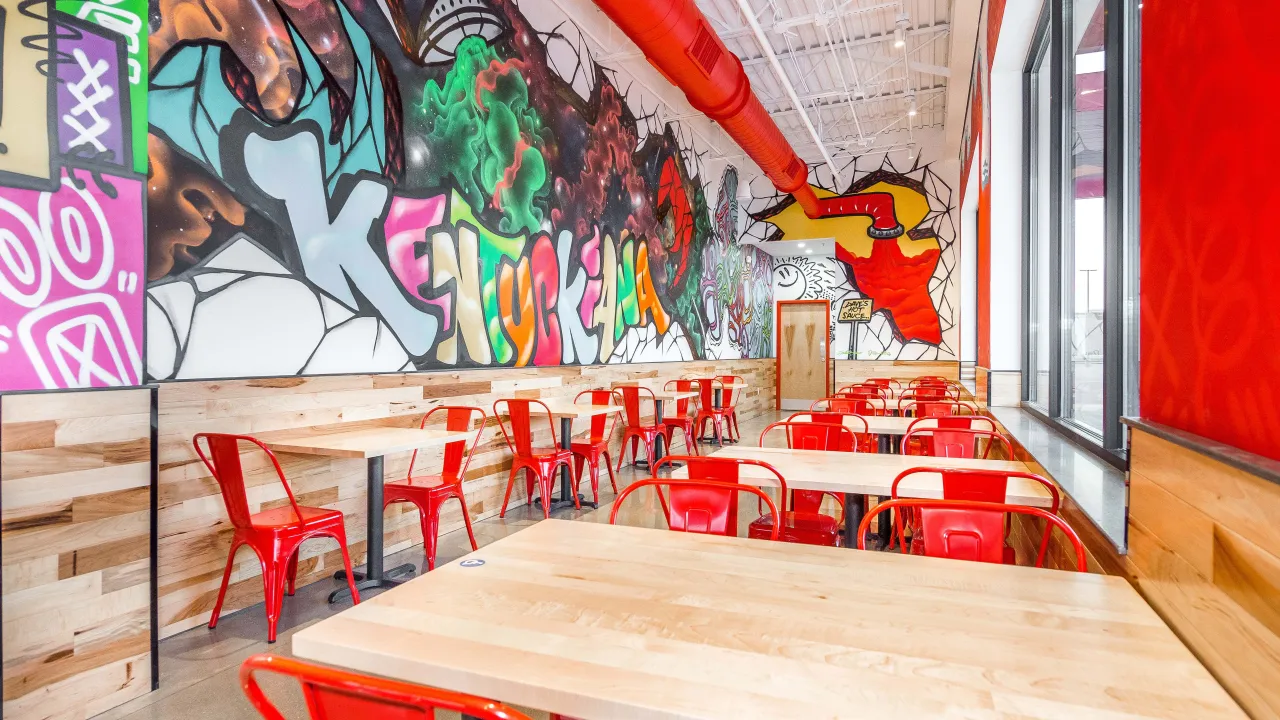 Interior view of Dave's Hot Chicken at 4125 Town Center Blvd, Jeffersonville, IN, showcasing vibrant murals and red seating.