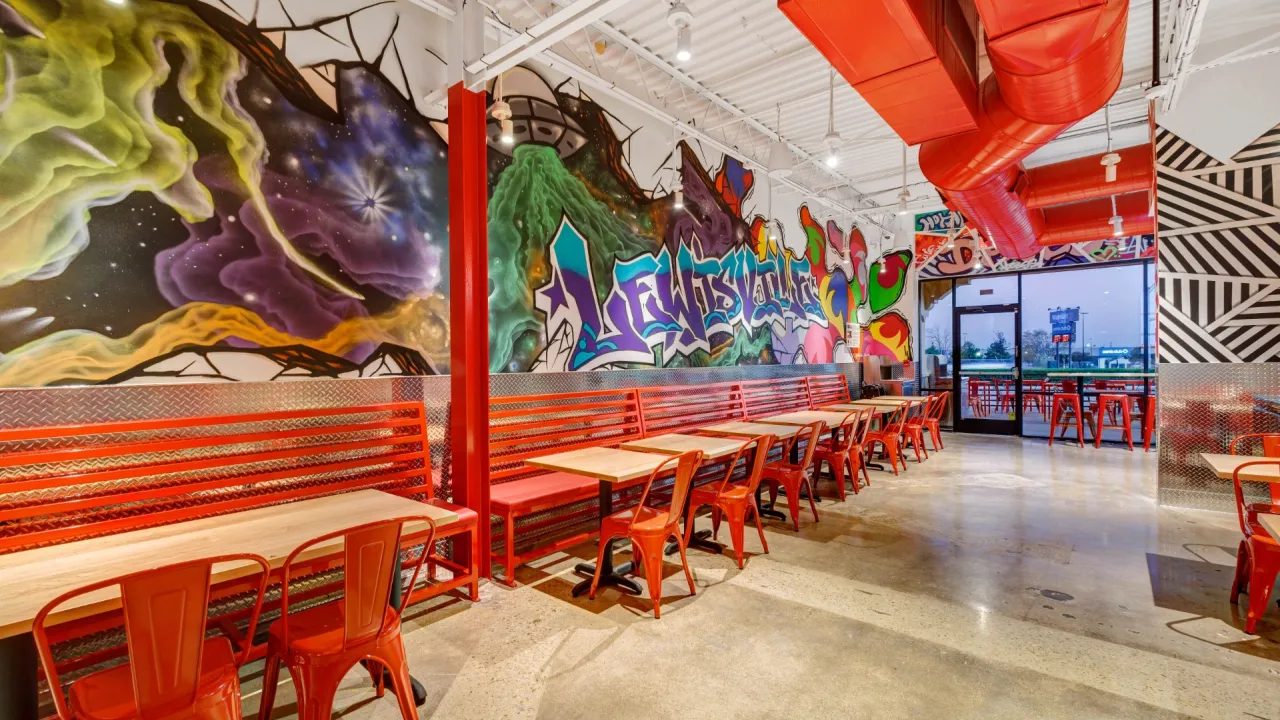 Interior view of Dave's Hot Chicken at 724 W Main St #500, Lewisville, TX, showcasing vibrant murals and red seating.