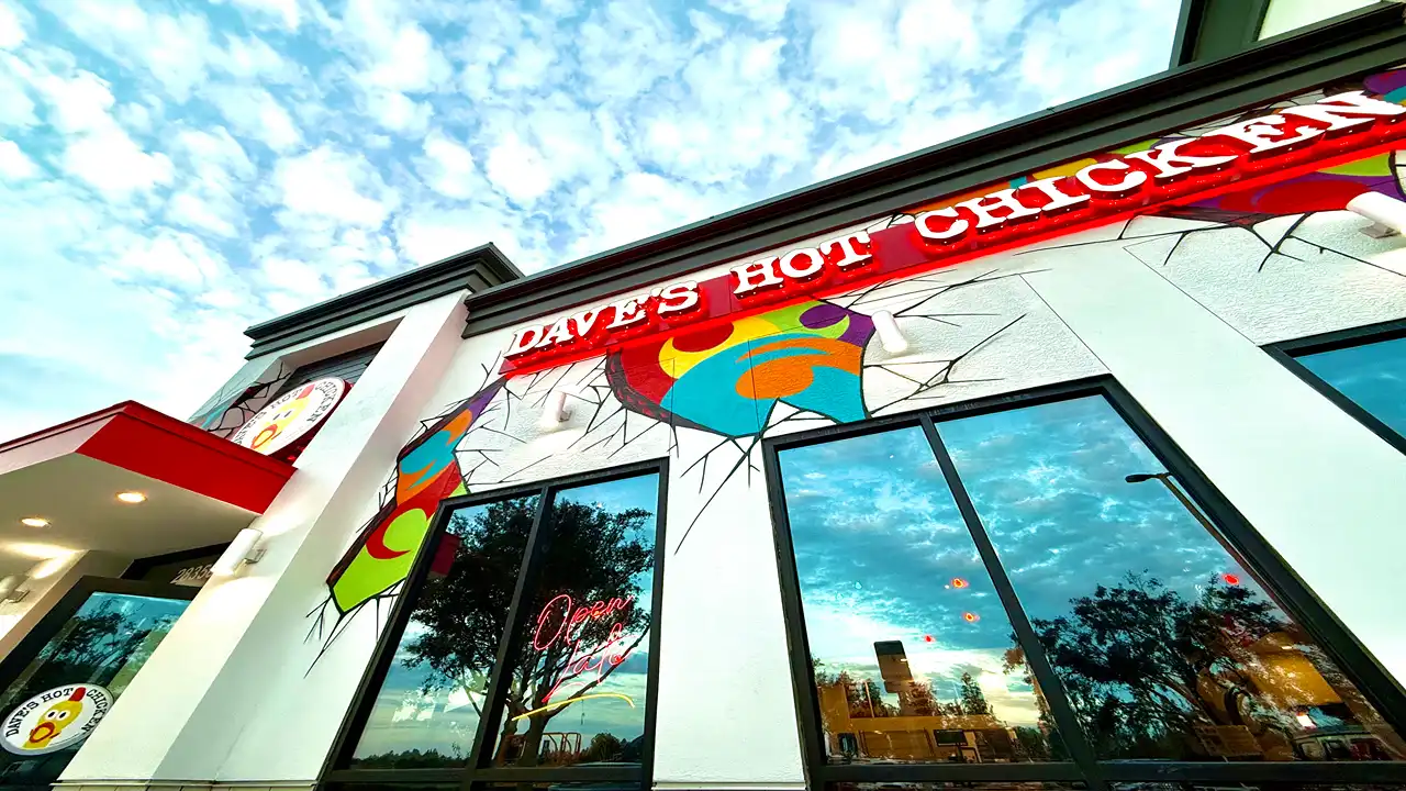 Angled exterior view of Dave’s Hot Chicken in Wesley Chapel, FL, showcasing colorful wall murals and red signage.