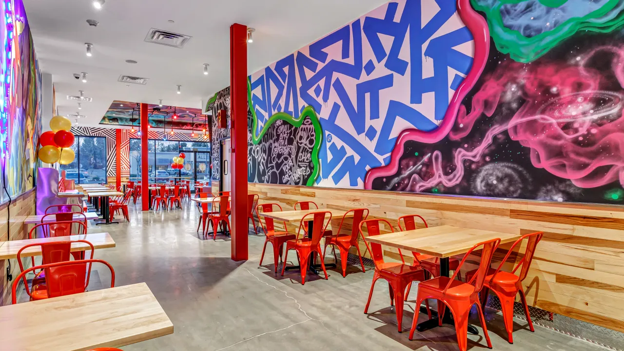 Interior view of Dave's Hot Chicken at 1611 Boston Post Rd, Milford, CT, showcasing vibrant murals and red seating.