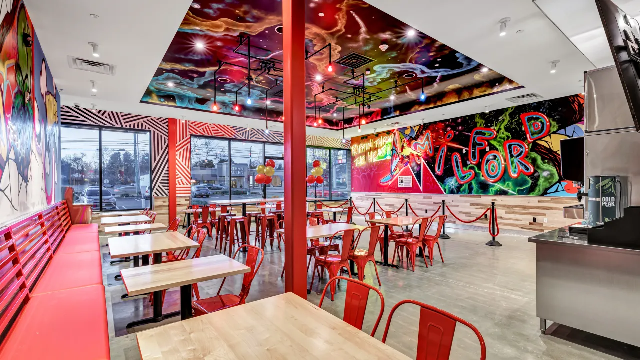 Interior view of Dave's Hot Chicken at 1611 Boston Post Rd, Milford, CT, showcasing colorful murals and vibrant seating.