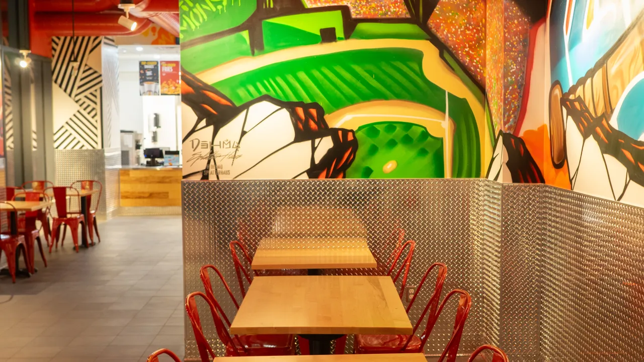 Interior view of Dave's Hot Chicken on Boylston Street, Boston, MA, showcasing vibrant murals and red seating.