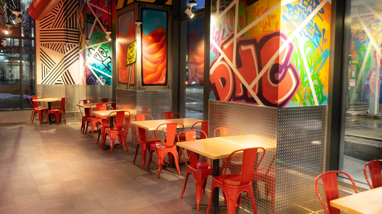 Interior view of Dave's Hot Chicken at 1260 Boylston Street, Boston, MA, showcasing vibrant murals and red metal chairs.