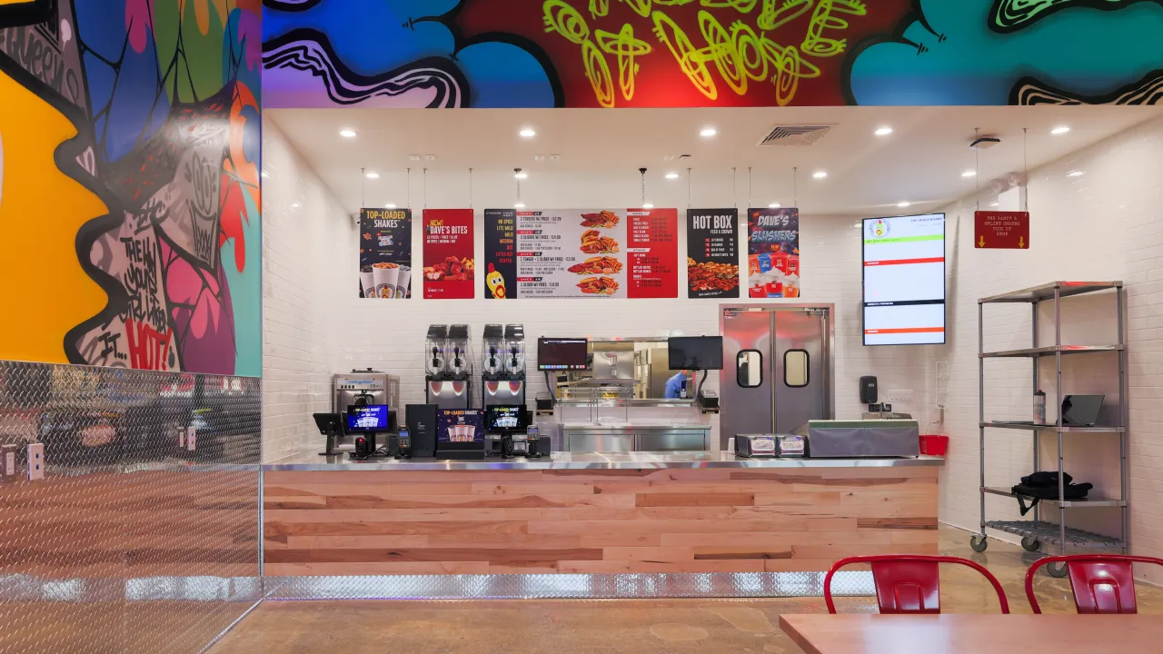 Interior view of Dave's Hot Chicken at 61-45 188th St, Fresh Meadows, NY, showcasing vibrant murals and a modern counter.