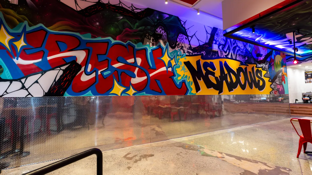 Interior view of Dave's Hot Chicken on 188th St, Fresh Meadows, NY, showcasing vibrant murals and a lively atmosphere.