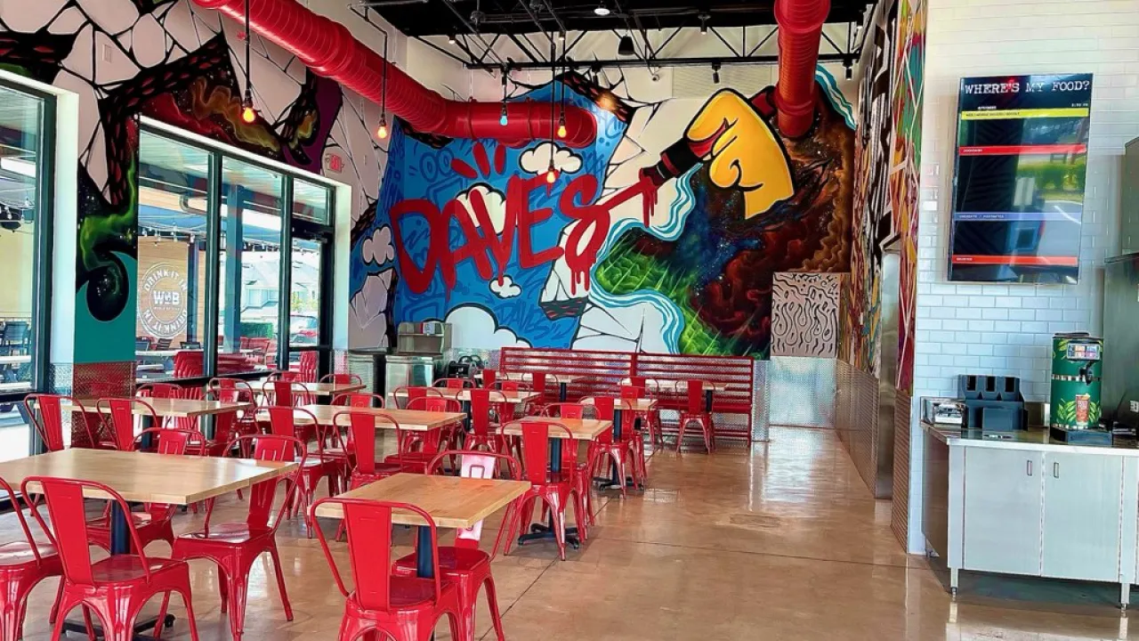 Interior view of Dave's Hot Chicken at 13446 Pine Gap Spur, Odessa, FL, showcasing vibrant murals and red metal furniture.