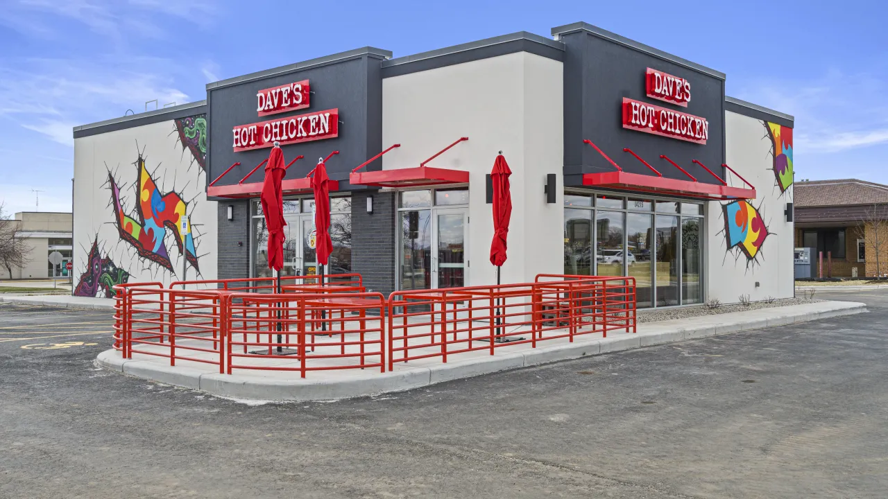 Exterior view of Dave's Hot Chicken at 4215 W. Wisconsin Ave, Appleton, WI, featuring vibrant murals and red umbrellas.