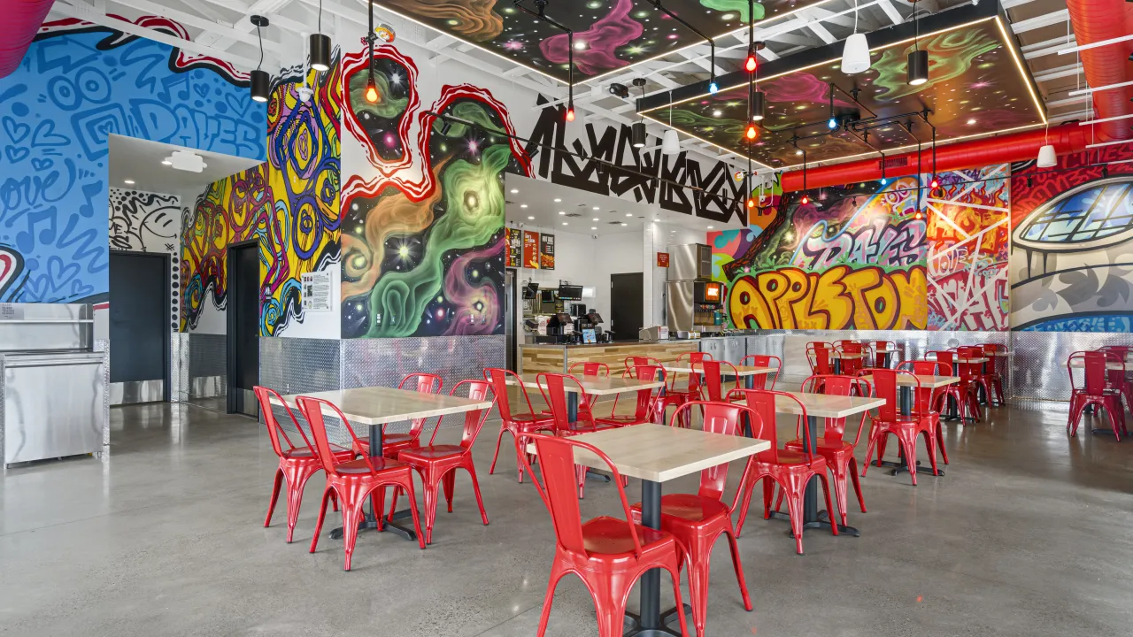 Interior view of Dave's Hot Chicken at 4215 W Wisconsin Ave, Appleton, WI, showcasing colorful murals and red chairs.