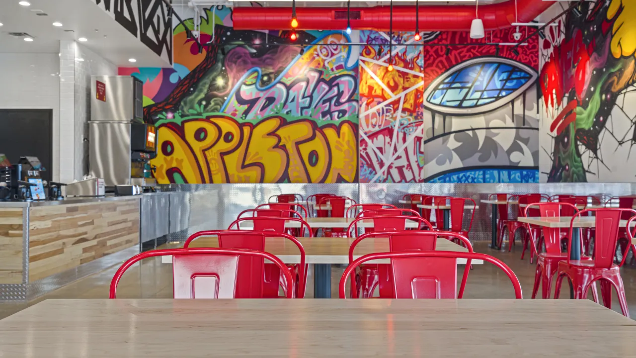 Interior view of Dave’s Hot Chicken at 4215 W. Wisconsin Ave, Appleton, WI, featuring vibrant graffiti and red seating.