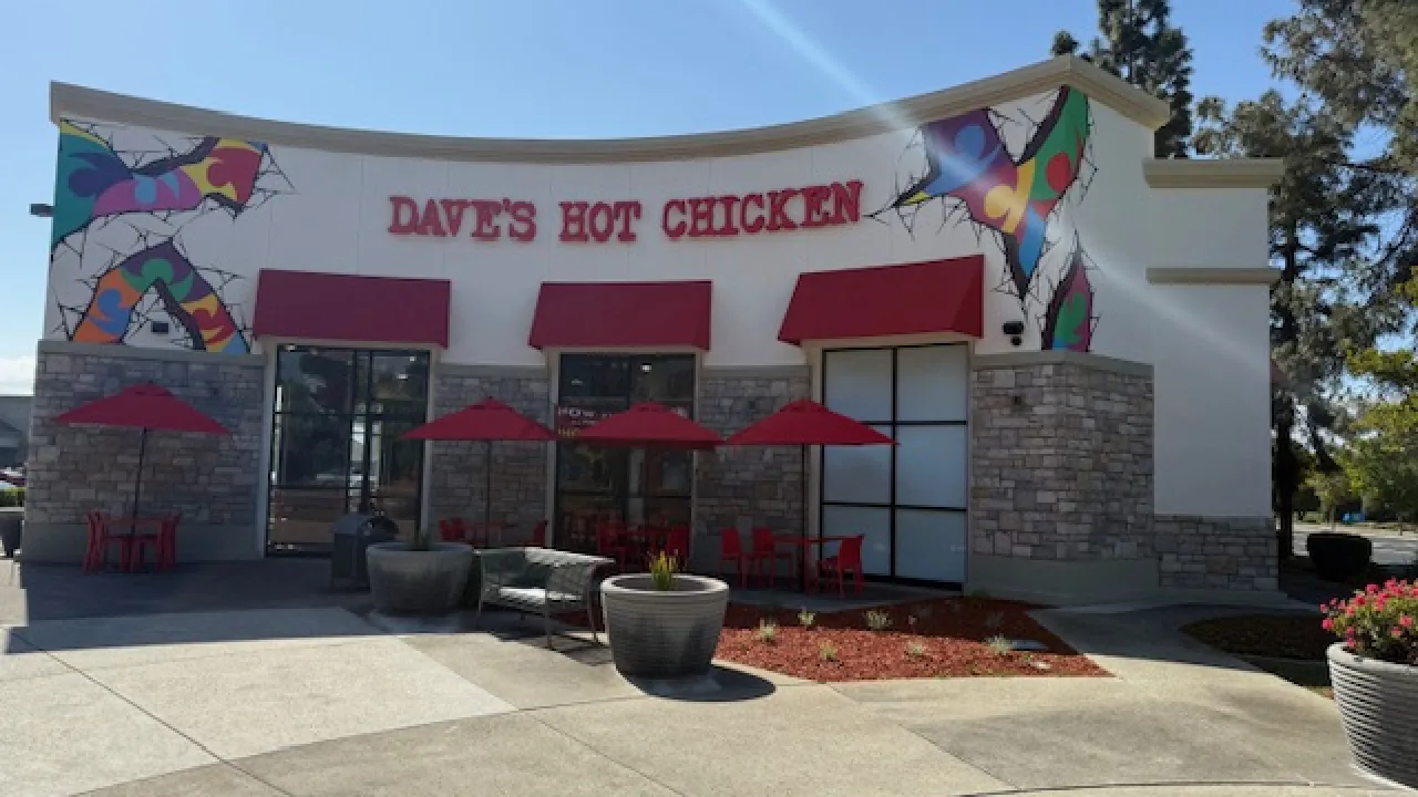 Exterior view of Dave's Hot Chicken on First St, Livermore, CA, showcasing colorful murals and red patio umbrellas.