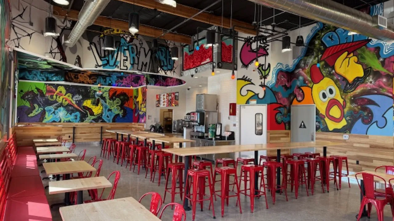 Interior view of Dave's Hot Chicken on First St, Livermore, CA, featuring vibrant murals and red metal seating.
