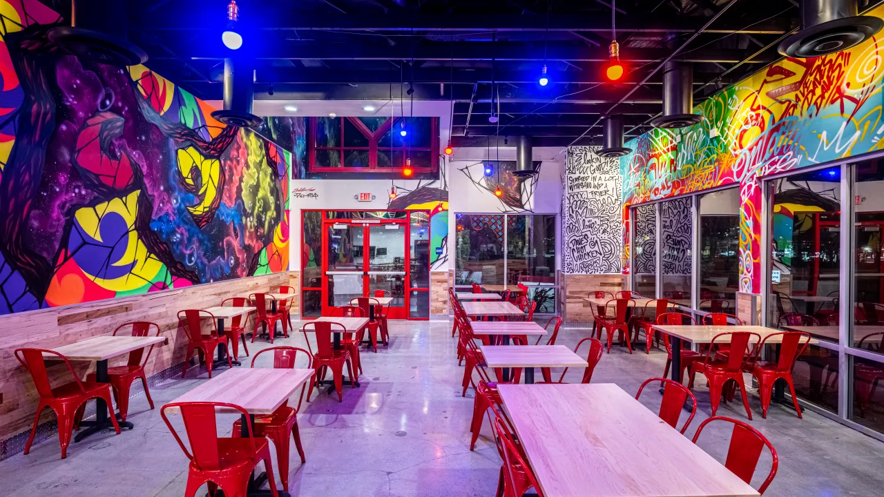 Interior view of Dave's Hot Chicken on Kingston Rd, Pickering, ON, showcasing colorful murals and red seating.