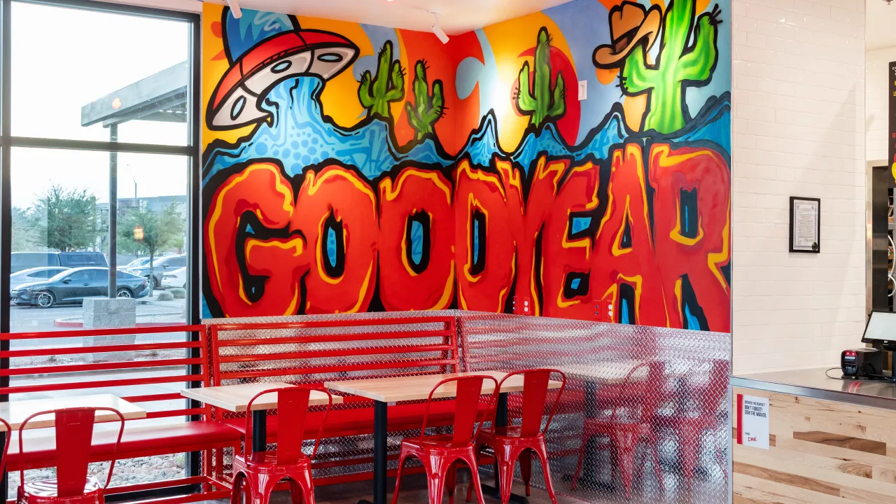 Interior view of Dave's Hot Chicken in Goodyear, AZ, showcasing vibrant murals and red seating.