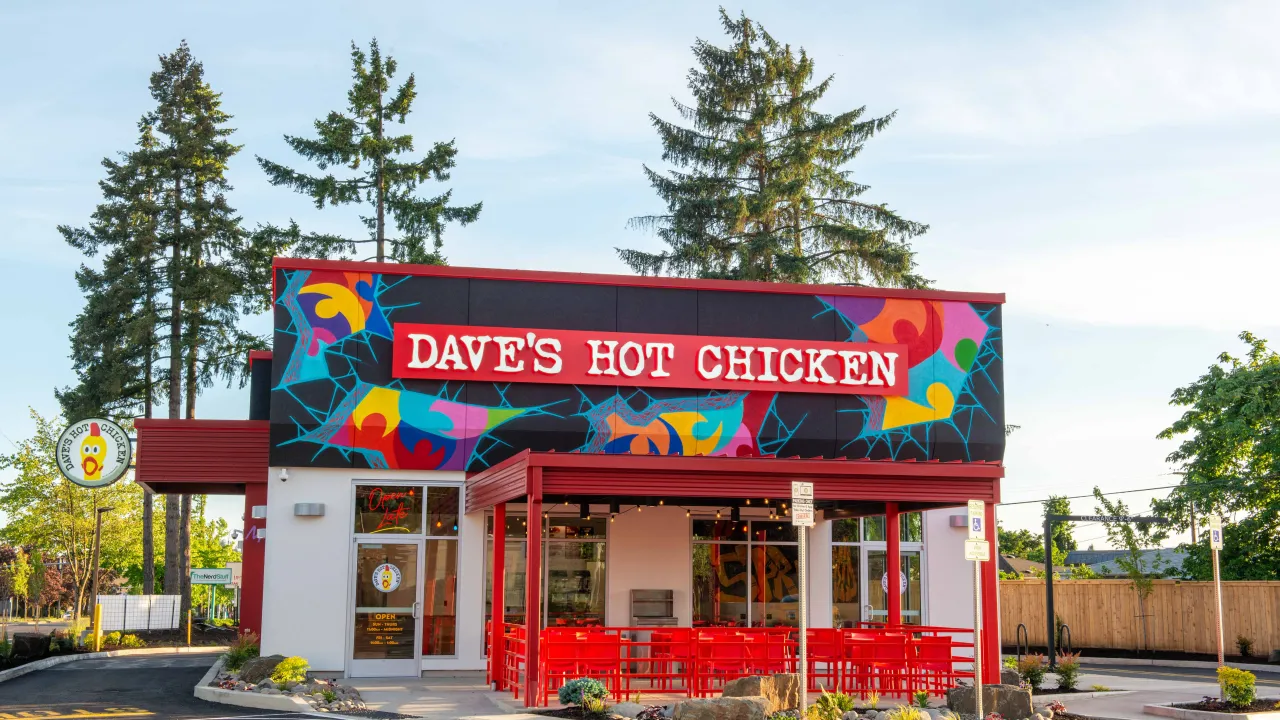 Exterior view of Dave's Hot Chicken on Mohawk Blvd, Springfield, OR, featuring vibrant mural and red outdoor seating.