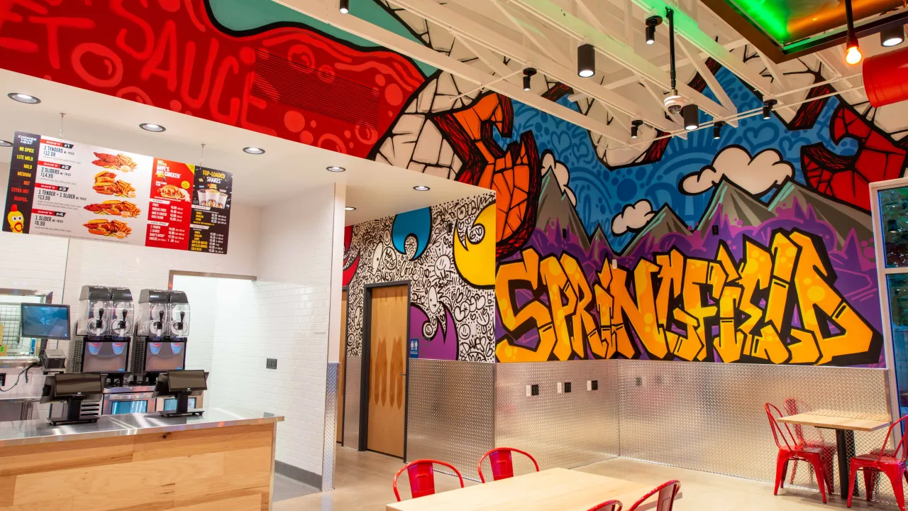 Interior view of Dave's Hot Chicken on Mohawk Blvd, Springfield, OR, showcasing vibrant murals and a modern counter.