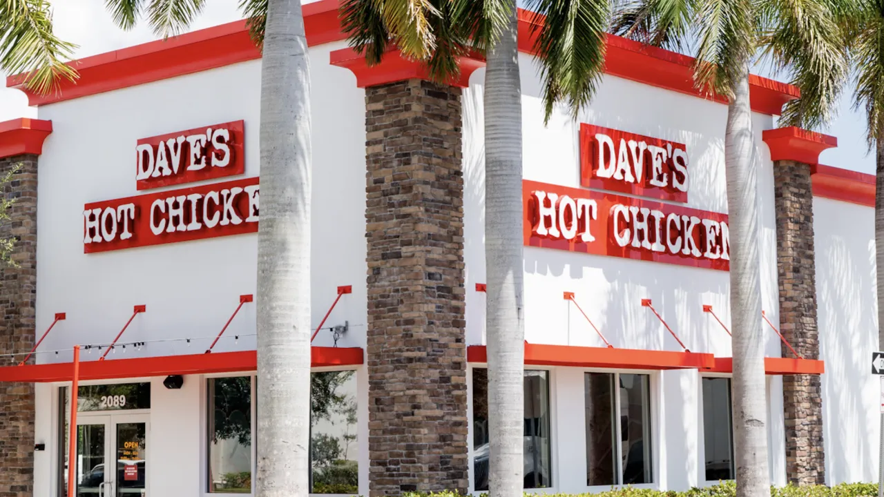 Exterior view of Dave's Hot Chicken at 2089 Palm Beach Lakes Blvd, West Palm Beach, FL, featuring red signage and palm trees.