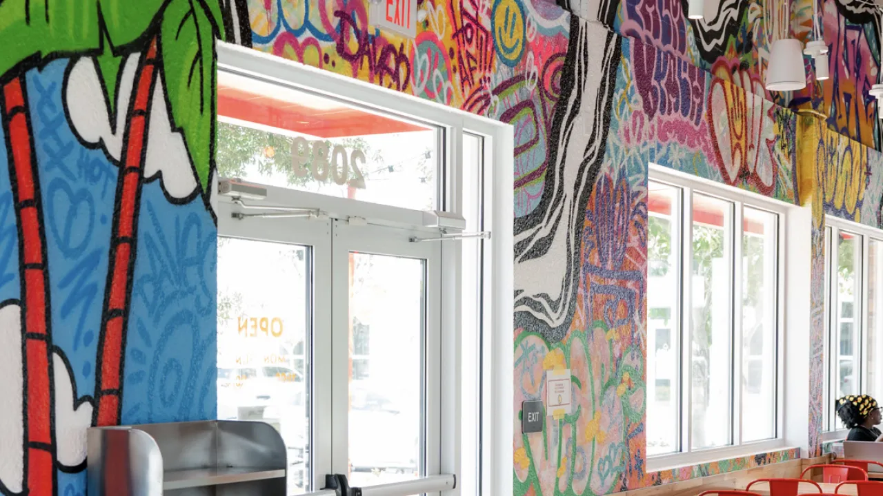Interior view of Dave's Hot Chicken on Palm Beach Lakes Blvd, West Palm Beach, FL, showcasing vibrant graffiti murals and bright ambiance.