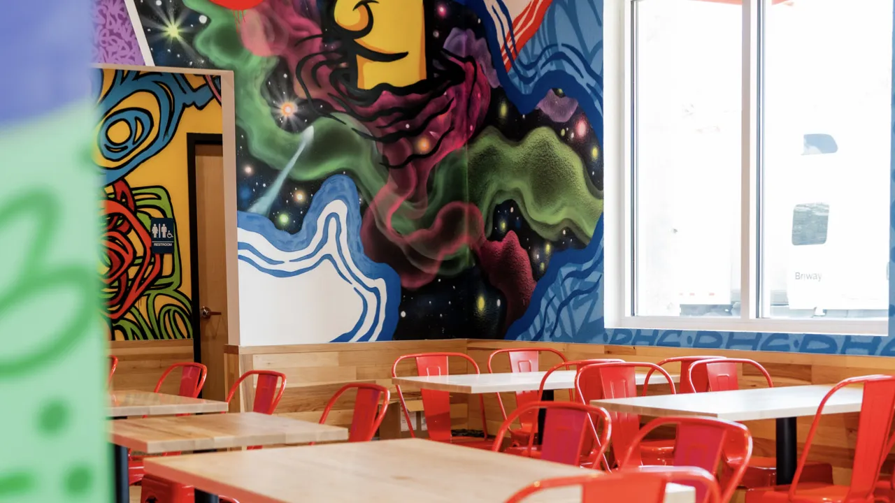 Interior view of Dave's Hot Chicken on Palm Beach Lakes Blvd, West Palm Beach, FL, showcasing vibrant murals and red seating.