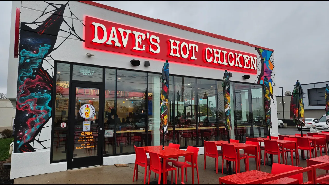 Exterior view of Dave's Hot Chicken at 1267 E. Ridge Rd, Rochester, NY, showcasing vibrant murals and red seating.