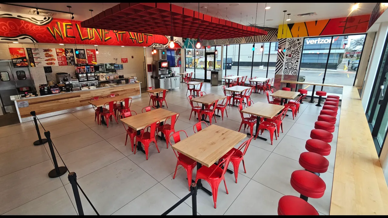 Interior view of Dave’s Hot Chicken on E. Ridge Rd, Rochester, NY, featuring red chairs, wooden tables, and vibrant murals.