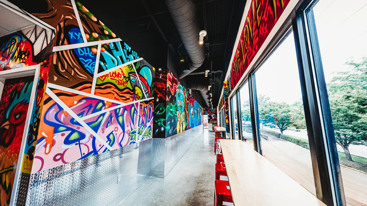 Interior view of Dave’s Hot Chicken on Roswell Road, Sandy Springs, GA, showcasing vibrant murals and casual seating.