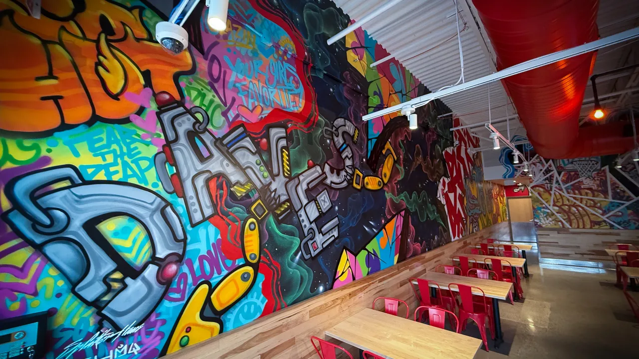 Interior view of Dave's Hot Chicken on N. Squirrel Rd, Auburn Hills, MI, showcasing vibrant murals and red seating.