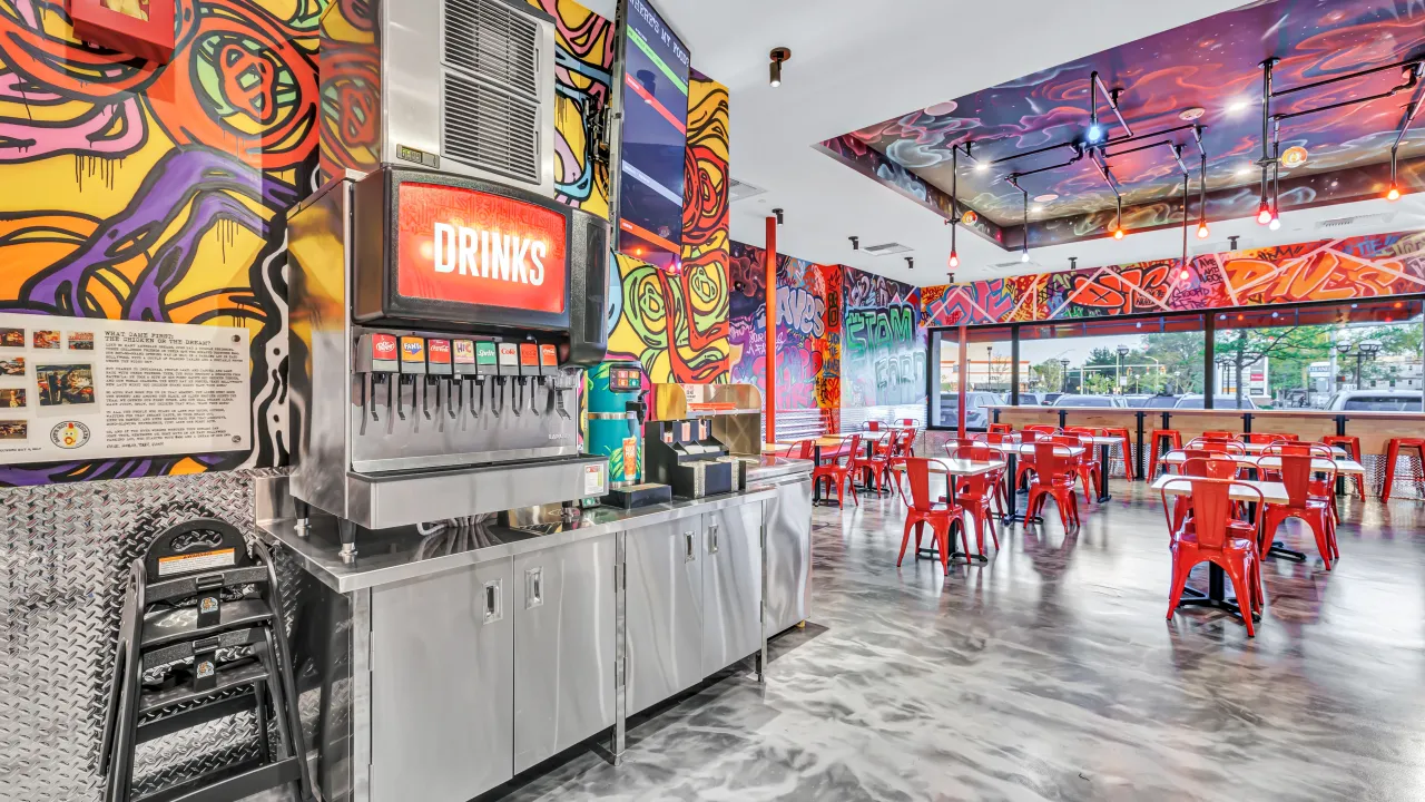 Interior view of Dave's Hot Chicken on Summer St, Stamford, CT, showcasing vibrant murals and red metal seating.