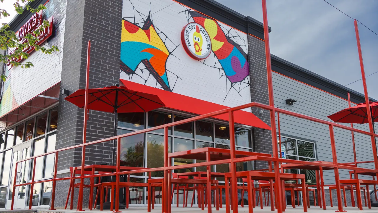 Exterior view of Dave's Hot Chicken at 2401 Wabash Ave, Springfield, IL, showcasing vibrant murals and red outdoor seating.