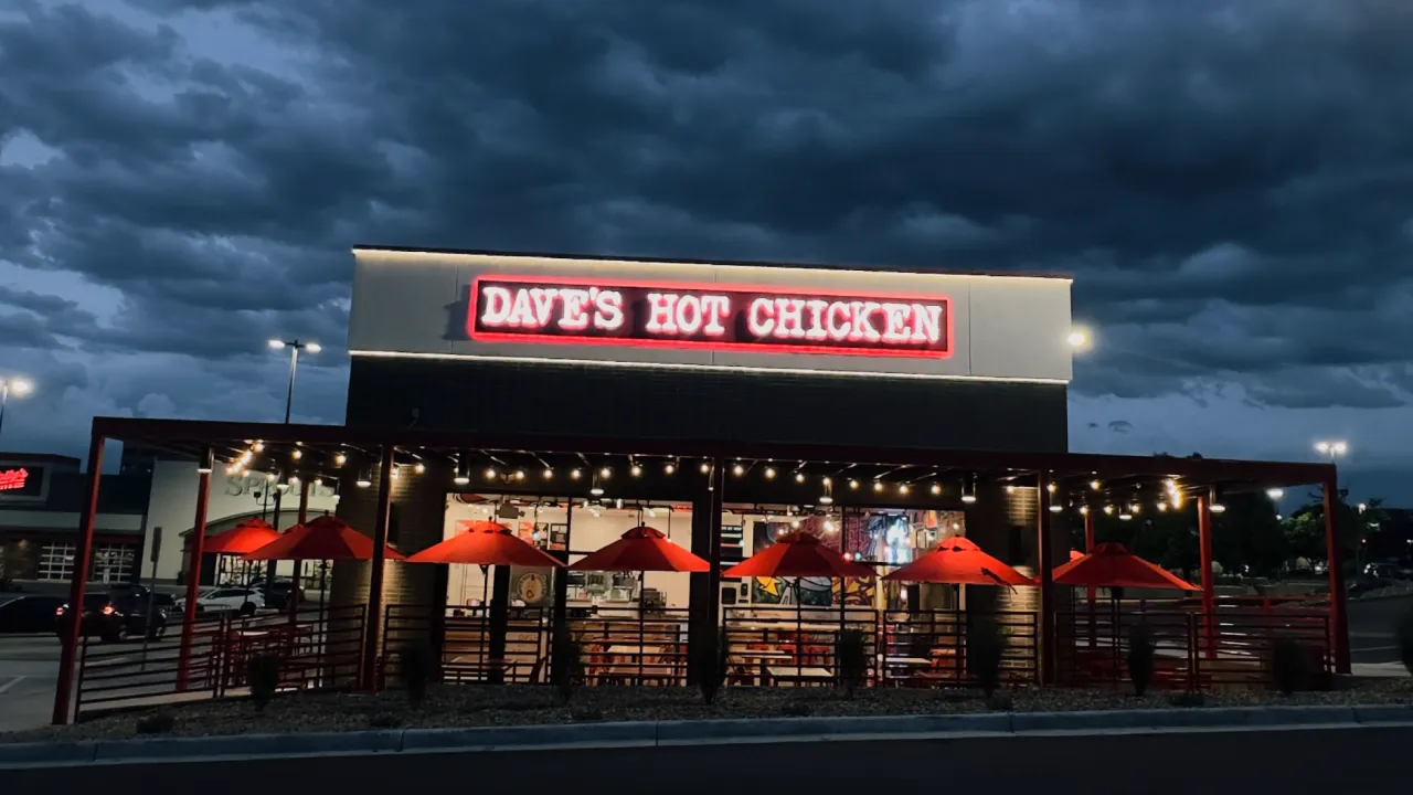 Exterior view of Dave’s Hot Chicken on E. Arapahoe Rd, Greenwood Village, CO, showcasing vibrant red umbrellas and neon signage.