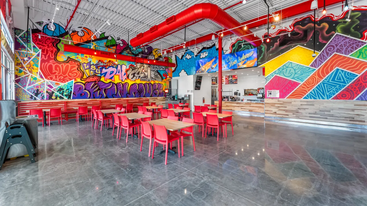 Interior view of Dave's Hot Chicken at 640 Arlington Creek Centre Dr, Baton Rouge, LA, showcasing vibrant murals and red seating.