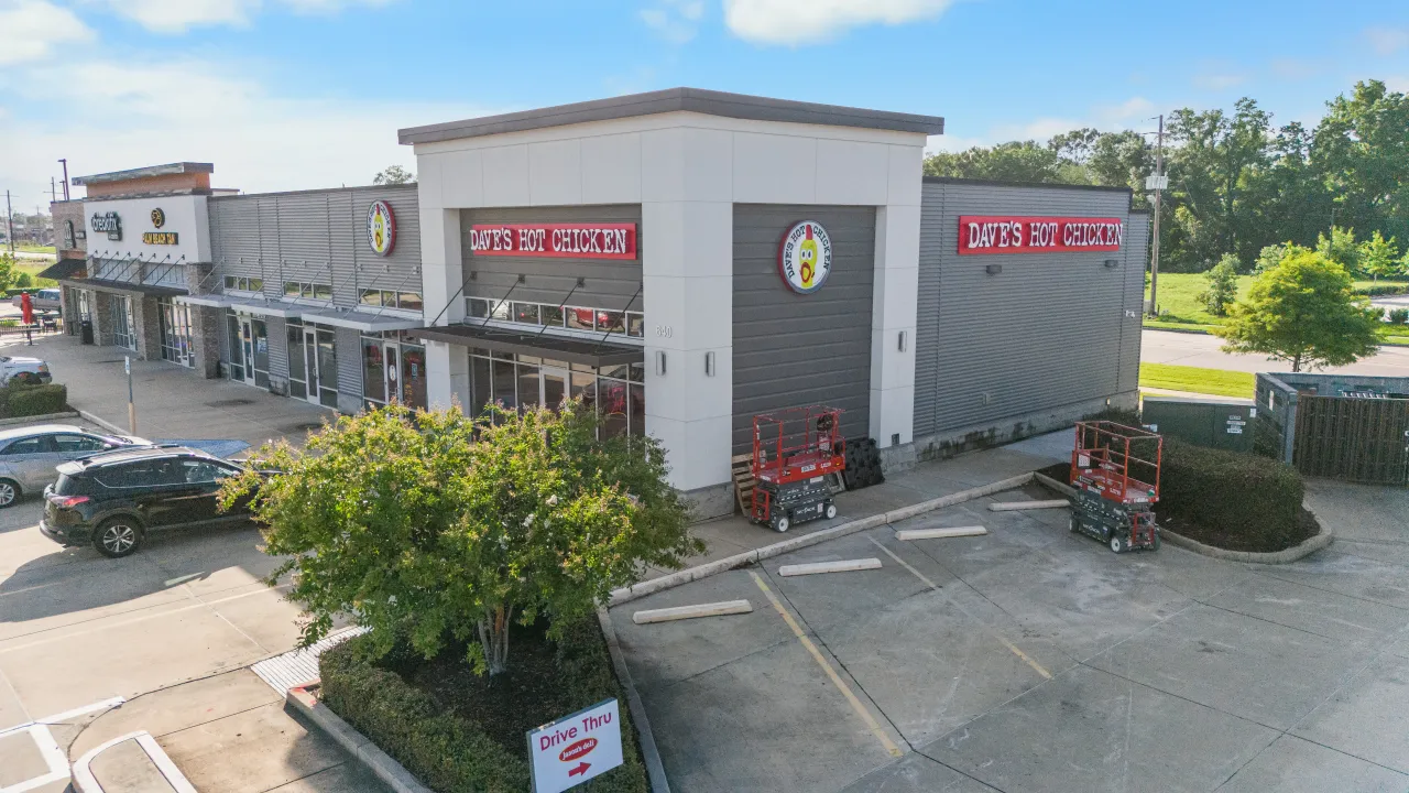 Exterior view of Dave's Hot Chicken at 640 Arlington Creek Centre Dr, Baton Rouge, LA, showcasing large red signage and greenery.