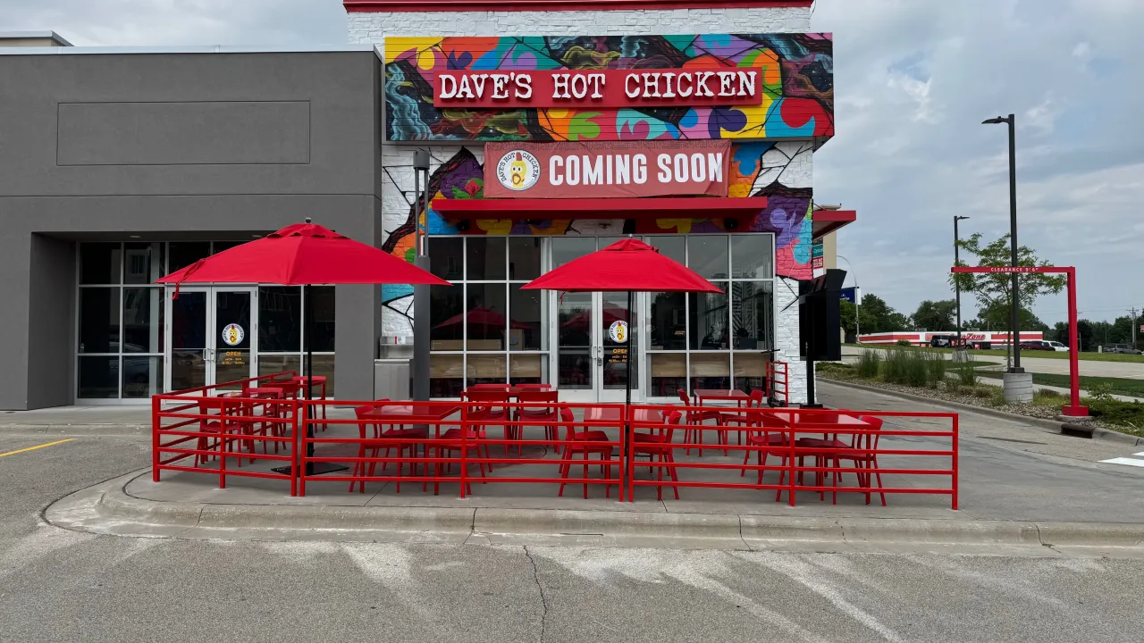 Exterior view of Dave's Hot Chicken on Broadway Ave, Rochester, MN, featuring colorful murals and red patio furniture.