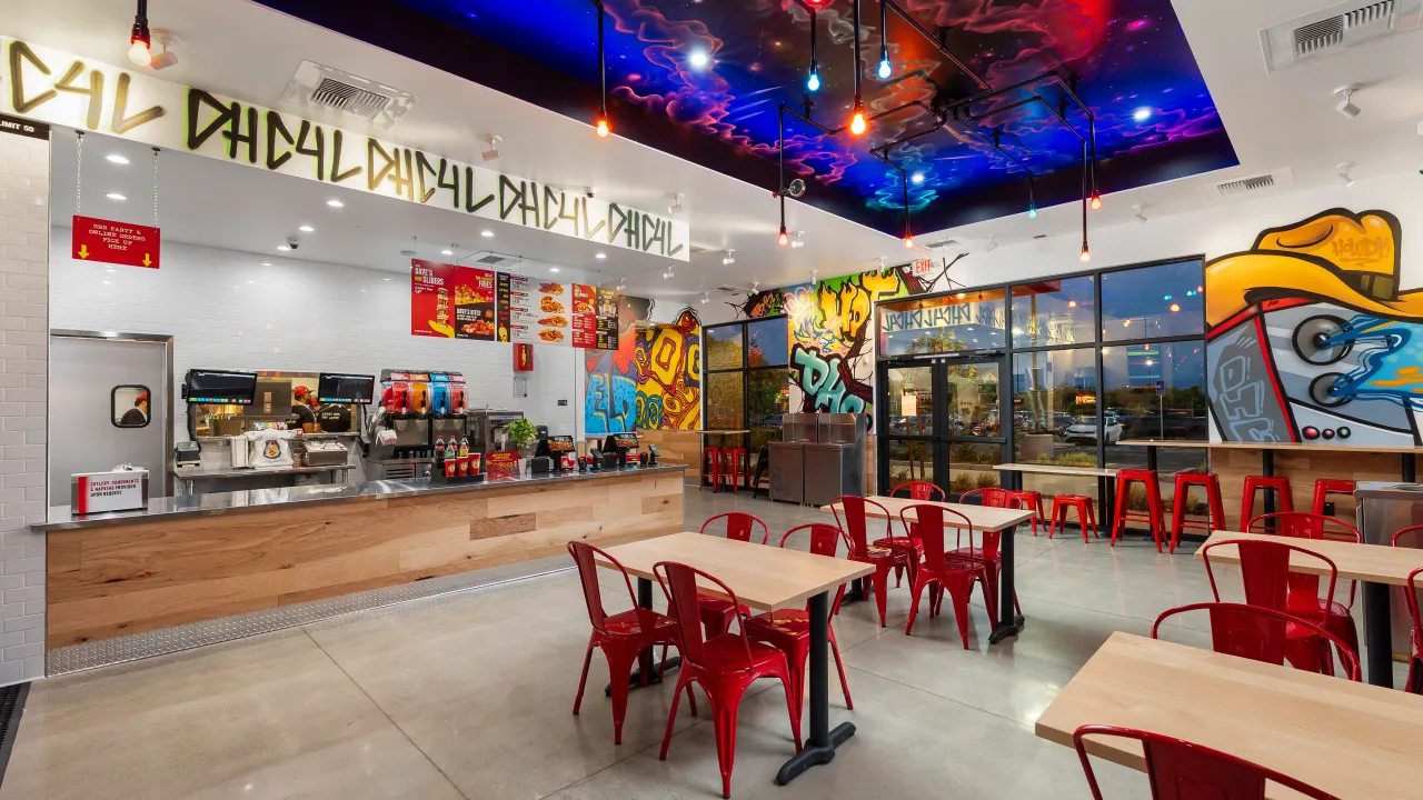Interior view of Dave’s Hot Chicken on Gosford Rd, Bakersfield, CA, showcasing vibrant murals and red chairs.