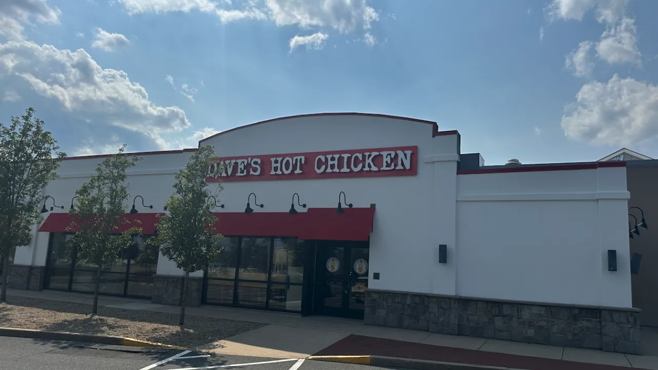 Exterior view of Dave's Hot Chicken on Providence Highway, Dedham, MA, showcasing red signage and surrounding trees.