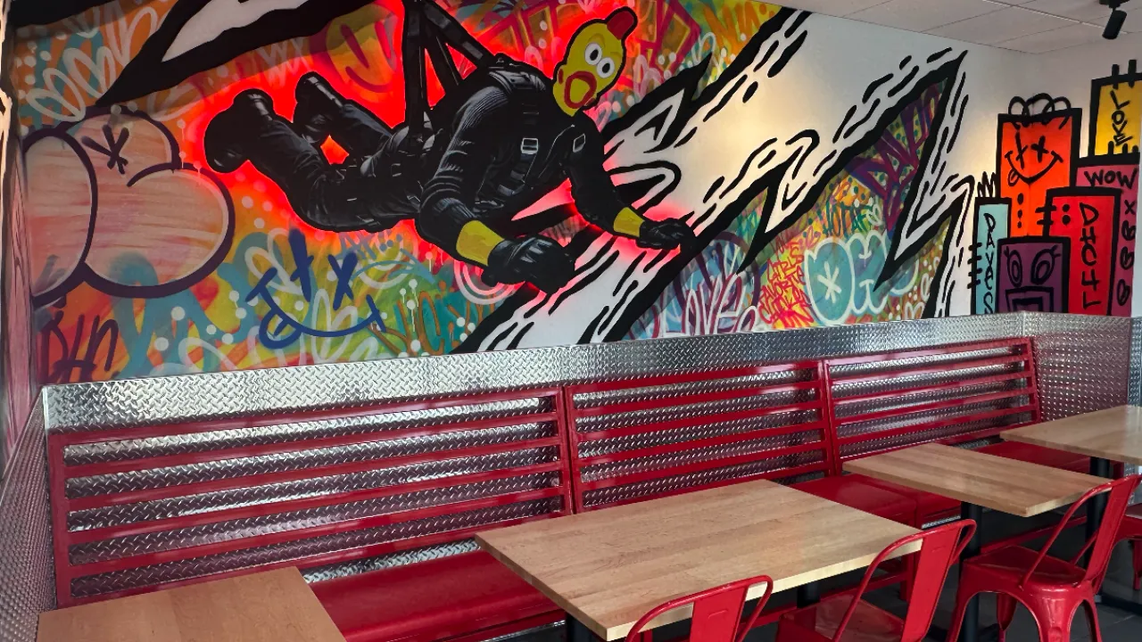 Interior view of Dave’s Hot Chicken at 797 Providence Highway, Dedham, MA, showcasing vibrant graffiti art and red seating.