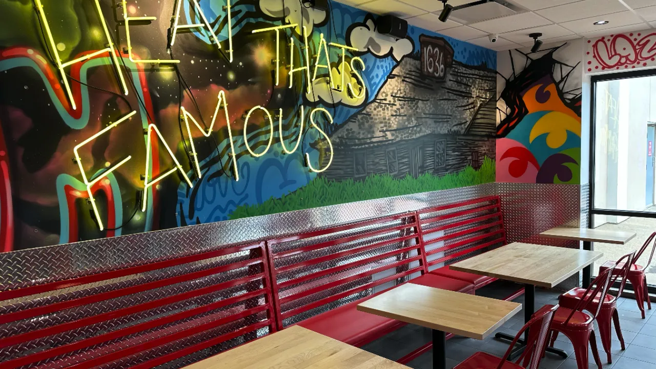 Interior view of Dave's Hot Chicken at 797 Providence Highway, Dedham, MA, showcasing vibrant murals and red seating.
