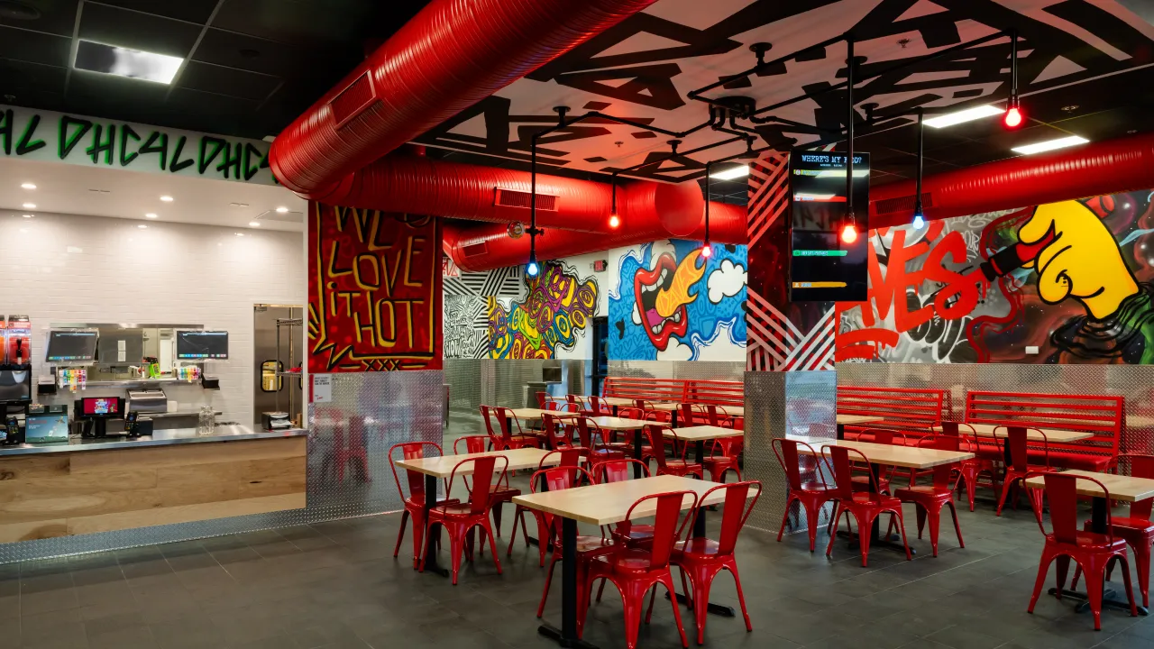 Interior view of Dave's Hot Chicken at 17304 Chesterfield Airport Rd, Chesterfield, MO, showcasing vibrant murals and red chairs.