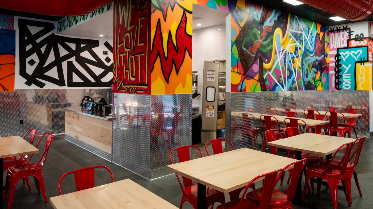 Interior view of Dave's Hot Chicken at 17304 Chesterfield Airport Rd, Chesterfield, MO, showcasing vibrant murals and red chairs.