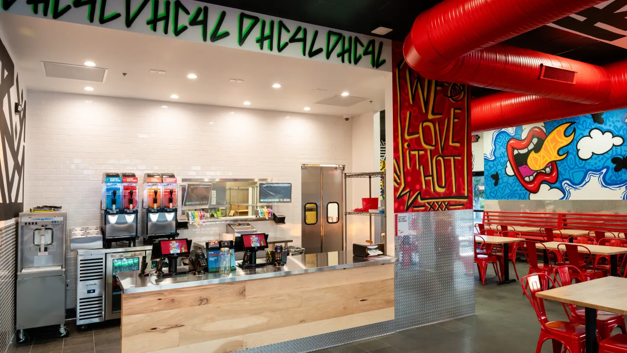 Interior view of Dave’s Hot Chicken at 17304 Chesterfield Airport Rd, Chesterfield, MO, showcasing vibrant murals and red seating.