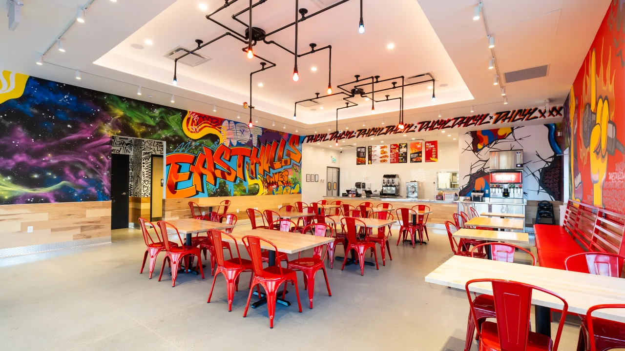 Interior view of Dave's Hot Chicken at 409 E. Hills Blvd SE #215, Calgary, AB, showcasing vibrant murals and red seating.